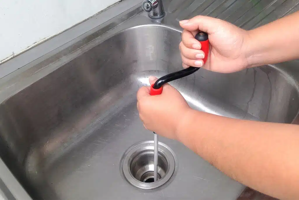 Frymire technician snaking a stainless steel kitchen sink drain in a Dallas, TX, home. 