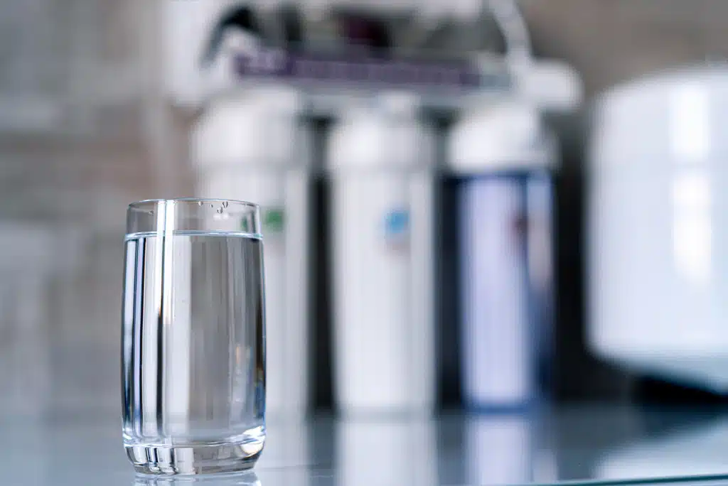 A glass of clean water with water filtration system in the background blurred in a home