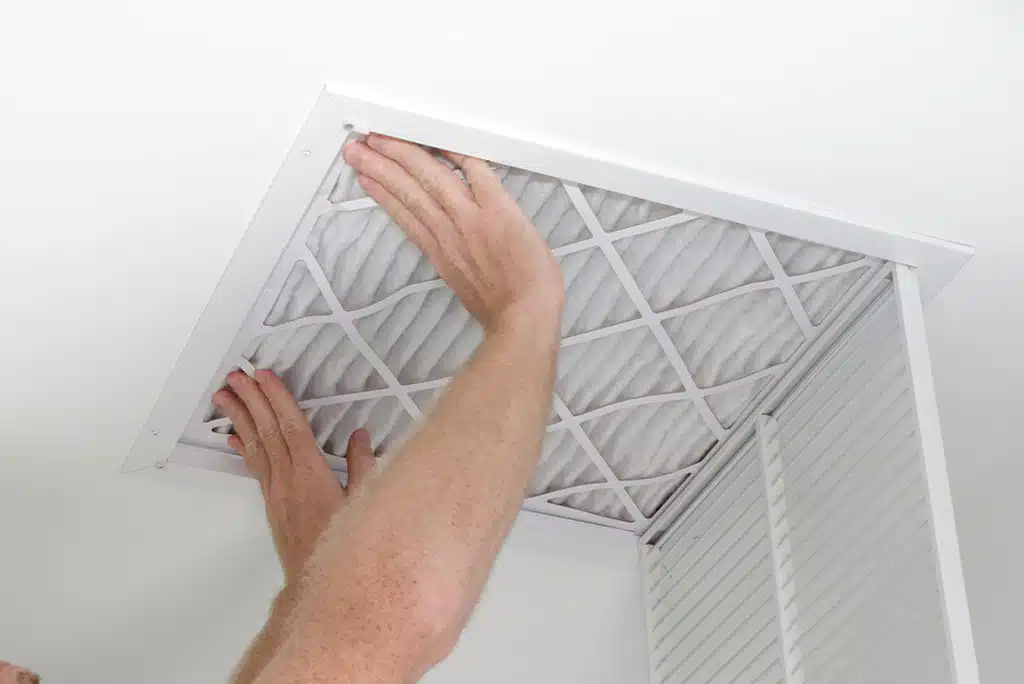 Technician's hands installing a clean HVAC filter in a home's white ceiling.
